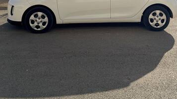 A white hatchback car parked on a paved area with a scenic view of mountains and a body of water in the background.