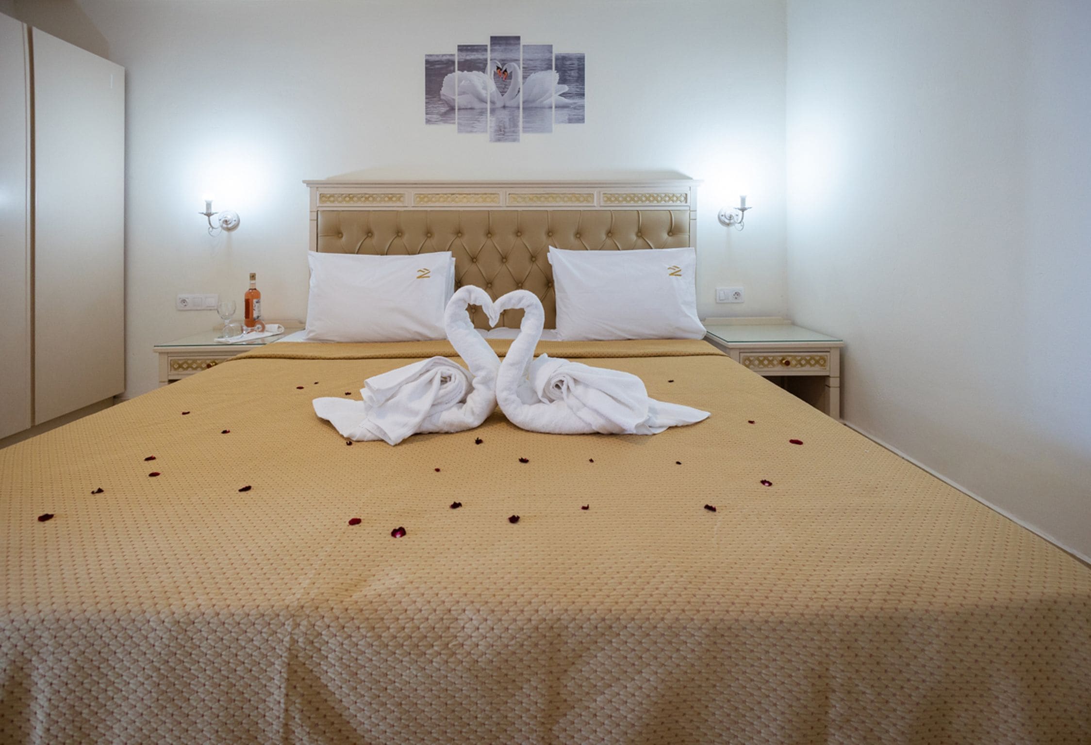 A hotel room with a large bed, two nightstands, a wall-mounted light, and a swan-themed artwork above the bed.