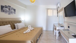 A hotel room with a large bed, a desk, a television, and an air conditioning unit.