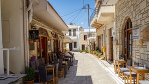 A narrow street with outdoor seating, stone buildings, and a café.