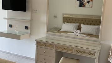 Una habitación de hotel con una cama, un tocador con espejo, un televisor montado en la pared y un cuadro sobre la cama.