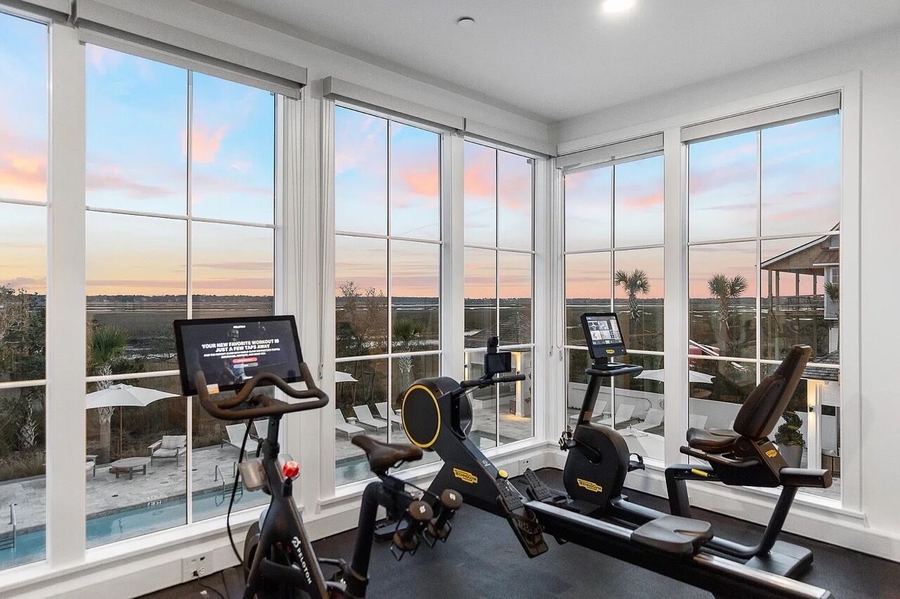 A gym with large windows, exercise equipment, and a view of a pool and landscape.