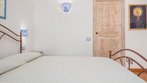 Un dormitorio con cama, una puerta de madera, una lámpara fijada a la pared y un cuadro enmarcado.