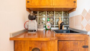 Una cocina con armarios de madera, una tetera, una botella de detergente y un fregadero.