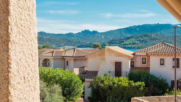 Un pueblo costero con arquitectura tradicional, un cielo azul brillante y montañas al fondo.