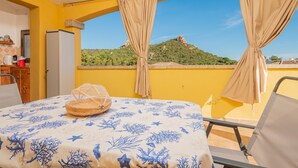 Una habitación con cama, una mesa con una cesta, una silla y un balcón con vistas a una colina.