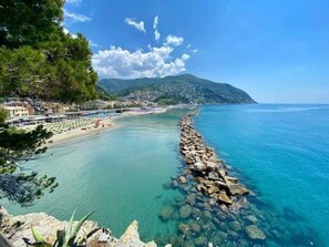 A coastal view with clear water, a rocky breakwater, and a building with a terrace.
