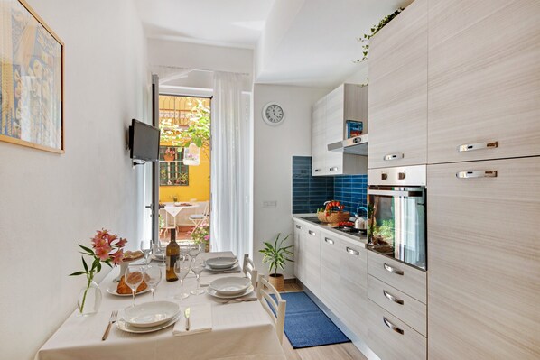 A compact kitchen with modern appliances, a dining area with a table set for four, and a view of the outside balcony.