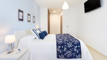 A bedroom with a bed, bedside table, lamp, wall-mounted TV, and framed pictures on the wall.