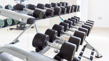 A gym with rows of dumbbells on racks, a treadmill, and a weight bench.