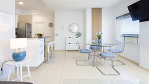 Une cuisine moderne équipée d’un réfrigérateur, un coin repas avec une table et des chaises en verre, et une grande fenêtre offrant une vue dégagée.
