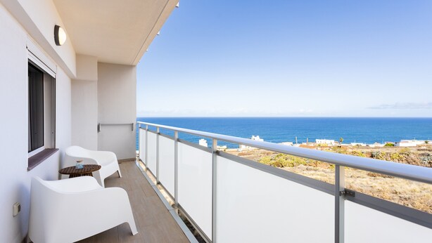 Un balcon avec des chaises blanches et une petite table, offrant une vue sur la côte.