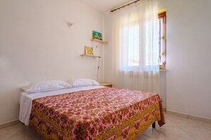 A bedroom with a bed, a window with curtains, and two wall-mounted shelves with pictures.