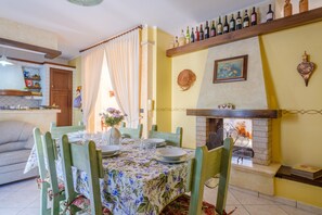 A dining area with a table set for four, a fireplace, and a shelf with wine bottles.