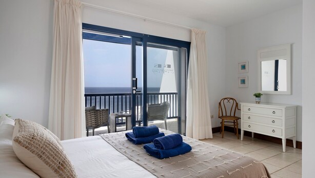 Een slaapkamer met een bed, een dressoir, een stoel en een balkon met uitzicht.