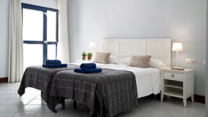 Een slaapkamer met een bed, twee nachtkastjes, een raam met gordijnen en een bedlampje.