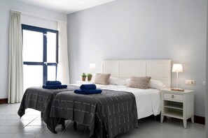 A bedroom with a bed, two bedside tables, a nightstand, a window with curtains, and a bedside lamp. - Villa 'Ajaches 23' with Sea View, Heated Pool, Balcony, A/C & Wi-Fi (Puerto Calero)