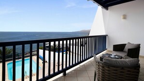 Een balkon met uitzicht op de zee, een zwembad en een zitgedeelte met een tafel.