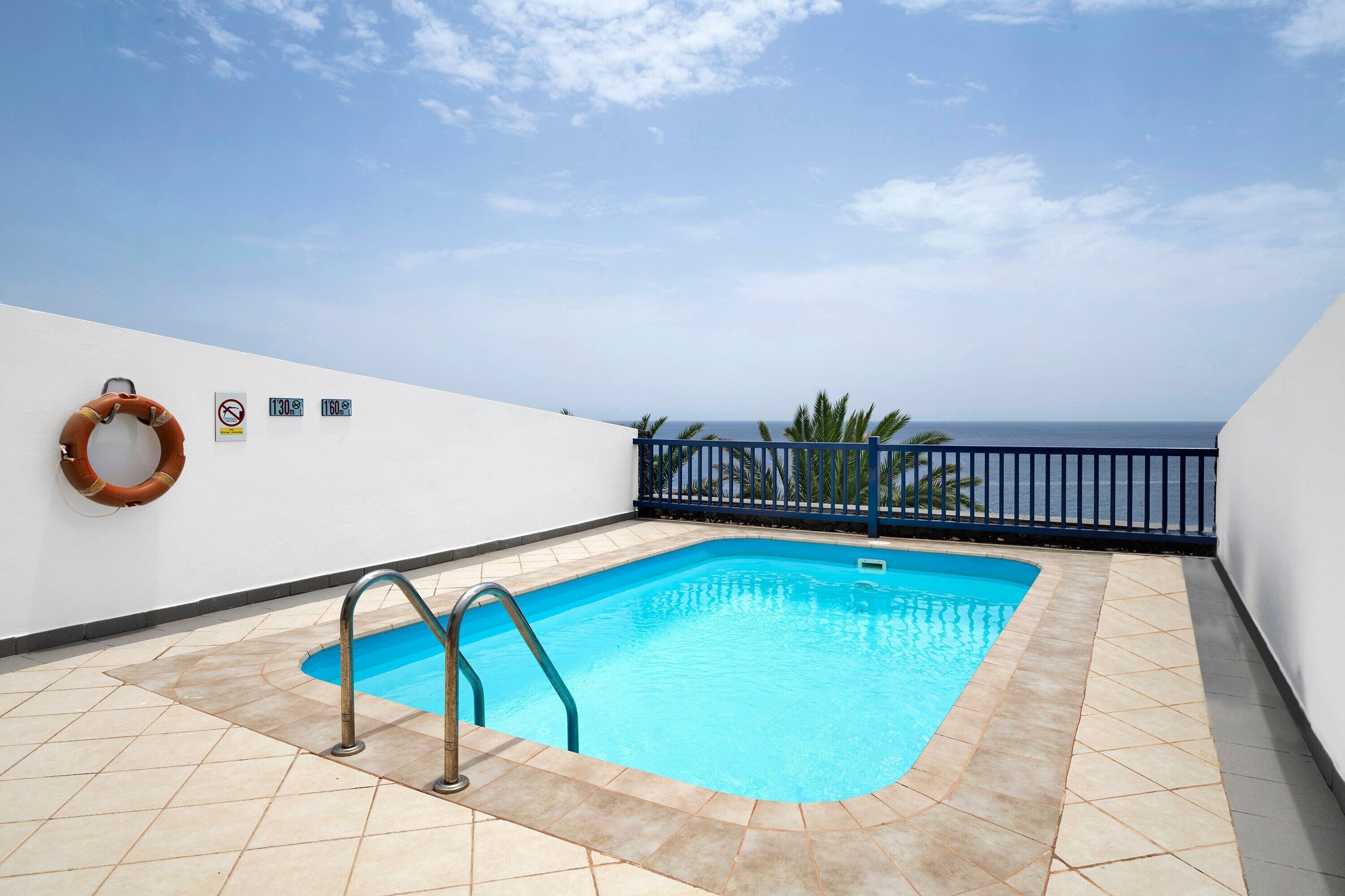 A rooftop swimming pool with a lifebuoy, a no diving sign, and a view of the ocean.