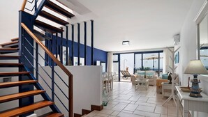 Een moderne woonkamer met een houten trap, een eethoek en grote ramen.