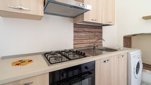 Une cuisine avec des meubles de rangement en bois, une cuisinière à gaz, un évier et un lave-linge.
