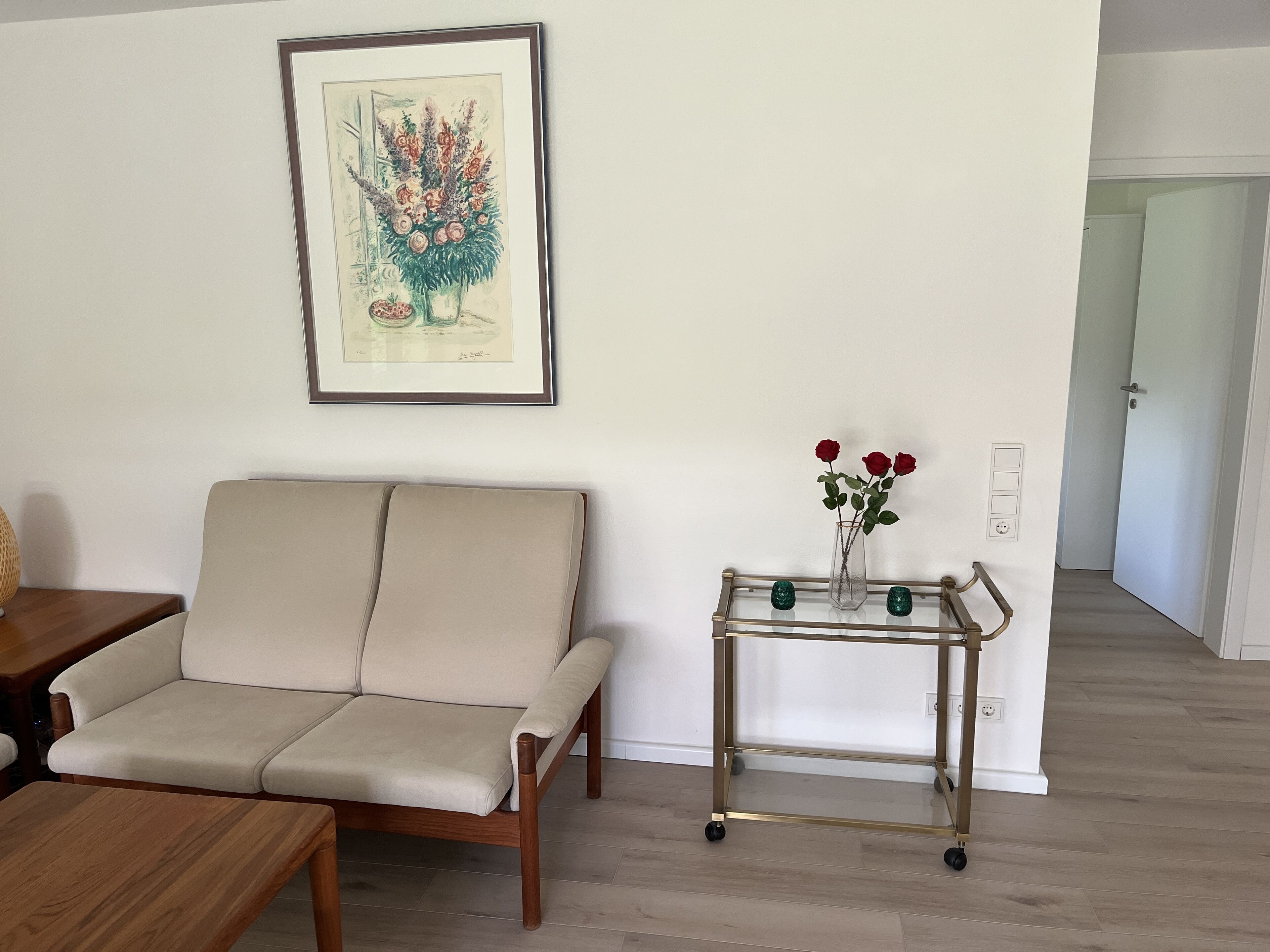 Een woonkamer met een bank, een salontafel, een kunstwerk in een lijst en een kleine tafel met een bloemenvaas.