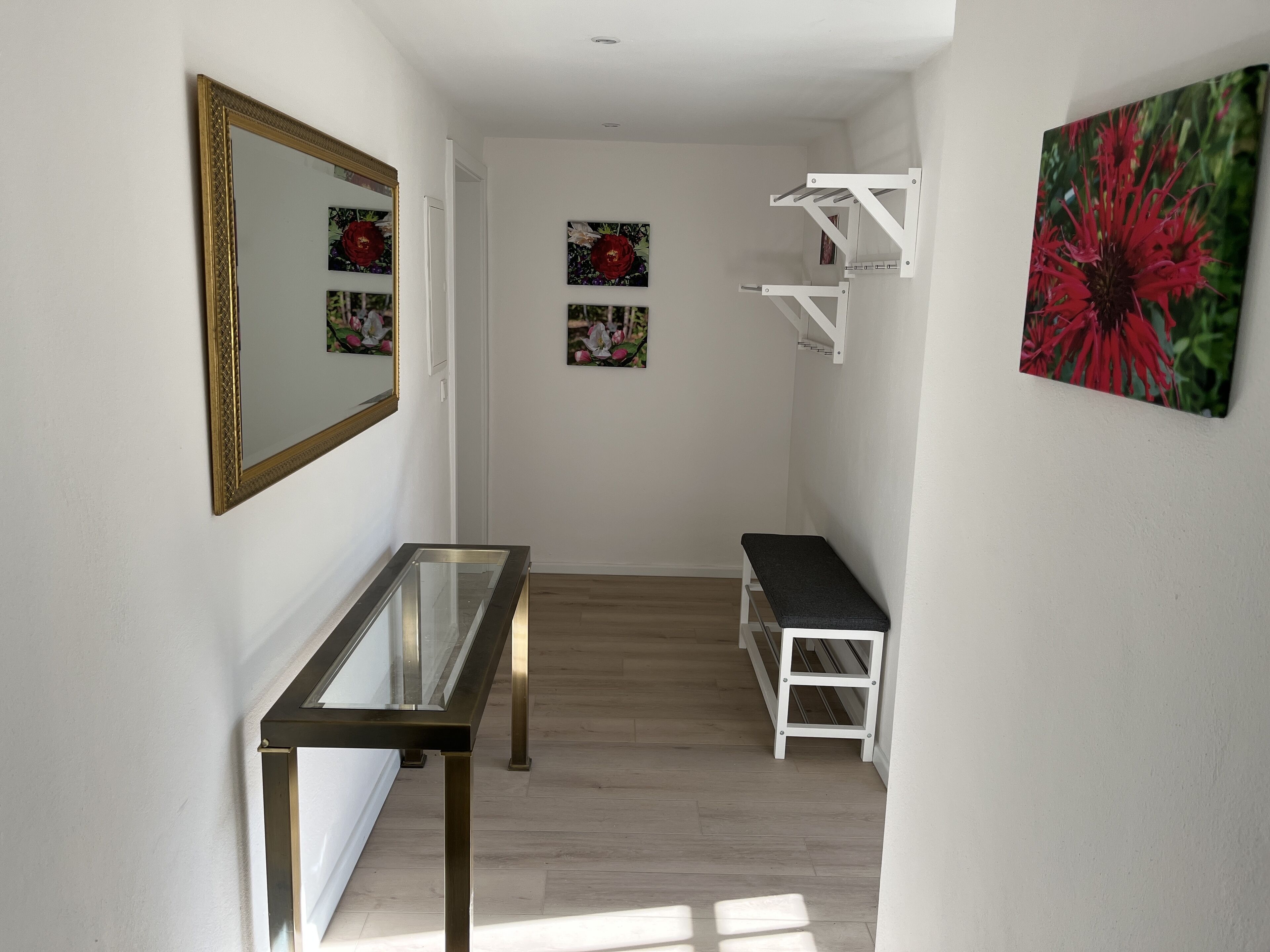 A hallway with a glass-top table, a bench, and wall-mounted shelves.