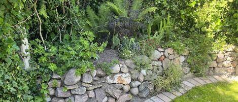 A garden with a stone wall, various plants, and a grassy area.