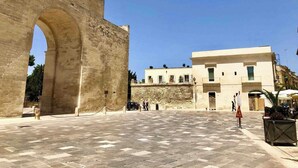 Un arco de piedra histórica que da acceso a un patio empedrado con un edificio al fondo.