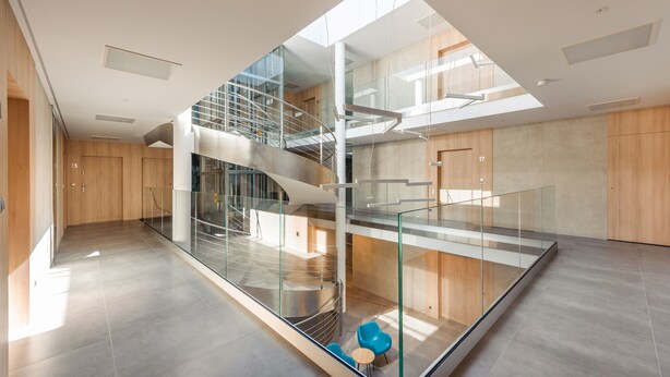 Un interior moderno con una escalera de cristal, una puerta de madera con la leyenda '13', y una silla azul.