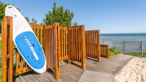 Una pasarela de madera que conduce a una playa con una tabla de surf apoyada en una valla.