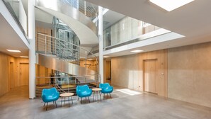 Un interior moderno con una escalera espiral central, puertas de madera y un área de estar con sillas azules.