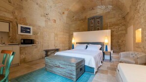 A bedroom with a stone wall, a bed with white linens, a nightstand, a lamp, and a small table. - Lu Leccio, Superior Suite Aqua (Lecce)