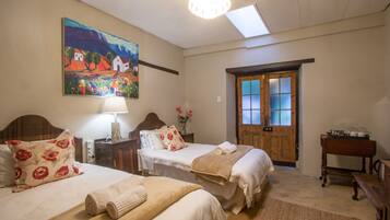 Habitación de hotel con dos camas, una puerta de madera, un candelabro y un cuadro en la pared.