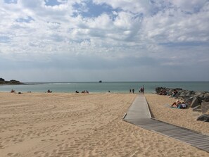 A sandy beach with a wooden walkway leading to the water, rocky outcrops, and people relaxing. - Feet in the water, between the beach, the pool, and the marina... (La Rochelle)