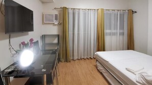 Una habitación con una cama, un escritorio con lámpara, un televisor y un equipo de aire acondicionado.
