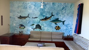 A living room with a sofa, a coffee table, and a wall mural of marine life. - Beach bed and Breakfast (Saquarema)