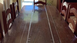A dining area with a wooden table and chairs, a view of the ocean through a glass door, and a small plant on the wall. - Beach bed and Breakfast (Saquarema)