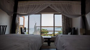 Un dormitorio con dos camas, un ventanal con vistas al mar y una estatua en el exterior.