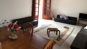 Una sala de estar con una mesa de comedor, sillas, un sofá, un televisor y techo de madera.