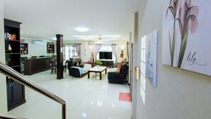 A spacious living area with a sofa, coffee table, and a TV. There are bookshelves and a staircase leading to another level. - Private Residence Hosted by Sasithorn (Pattaya)