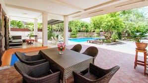 A covered patio area with a pool, wicker furniture, and a table with a vase of flowers. - Private Residence Hosted by Sasithorn (Pattaya)