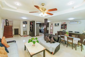 A spacious living area with a ceiling fan, a sofa, a dining table with chairs, and a kitchen in the background. - Private Residence Hosted by Sasithorn (Pattaya)