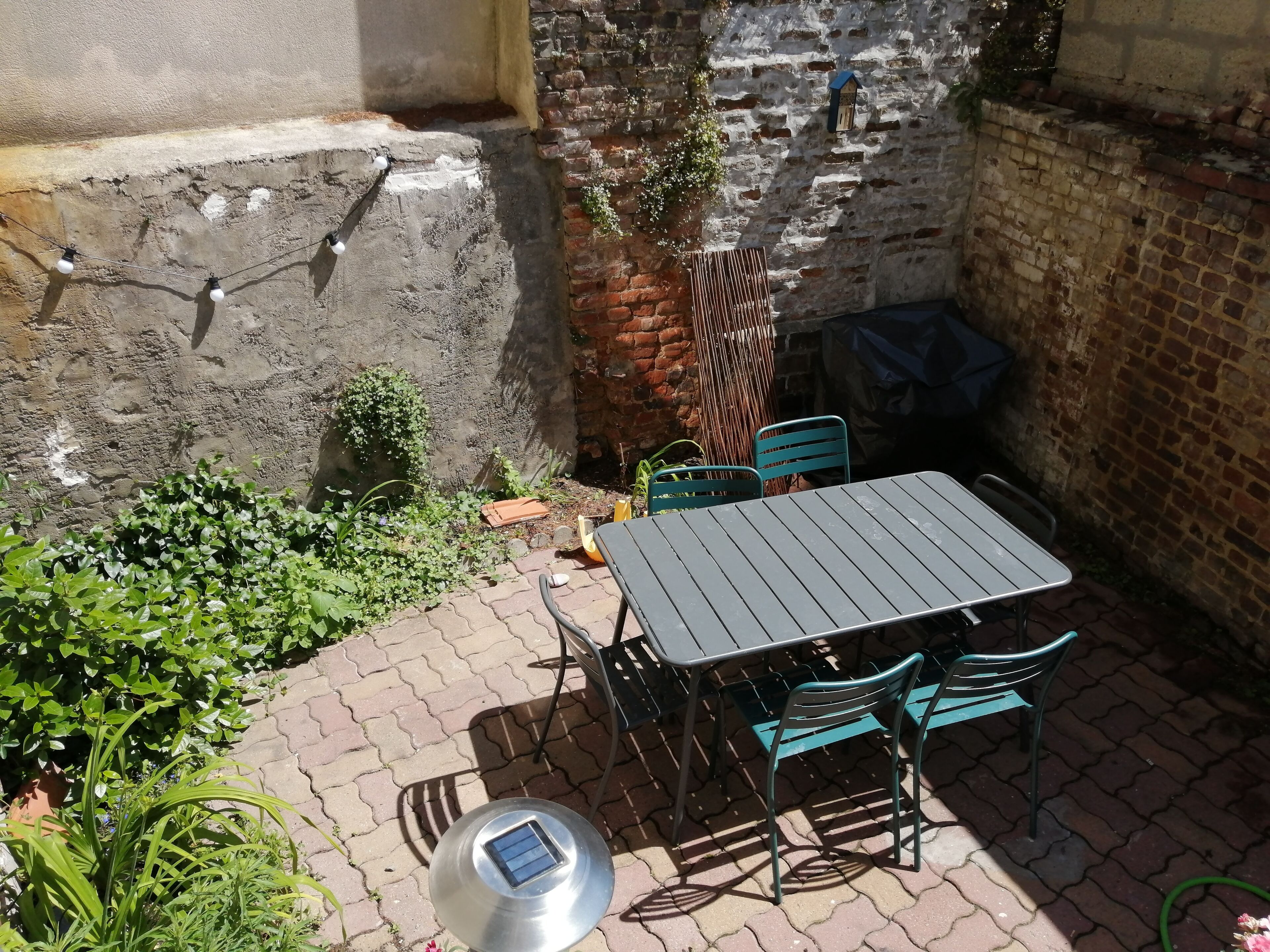 En terrasse med et bord, stole, en solcelledrevet enhed og en murstensmur.