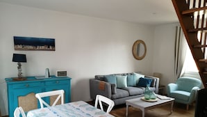 A cozy living room with a blue cabinet, a grey sofa, a white chair, and a small table with a lamp.
