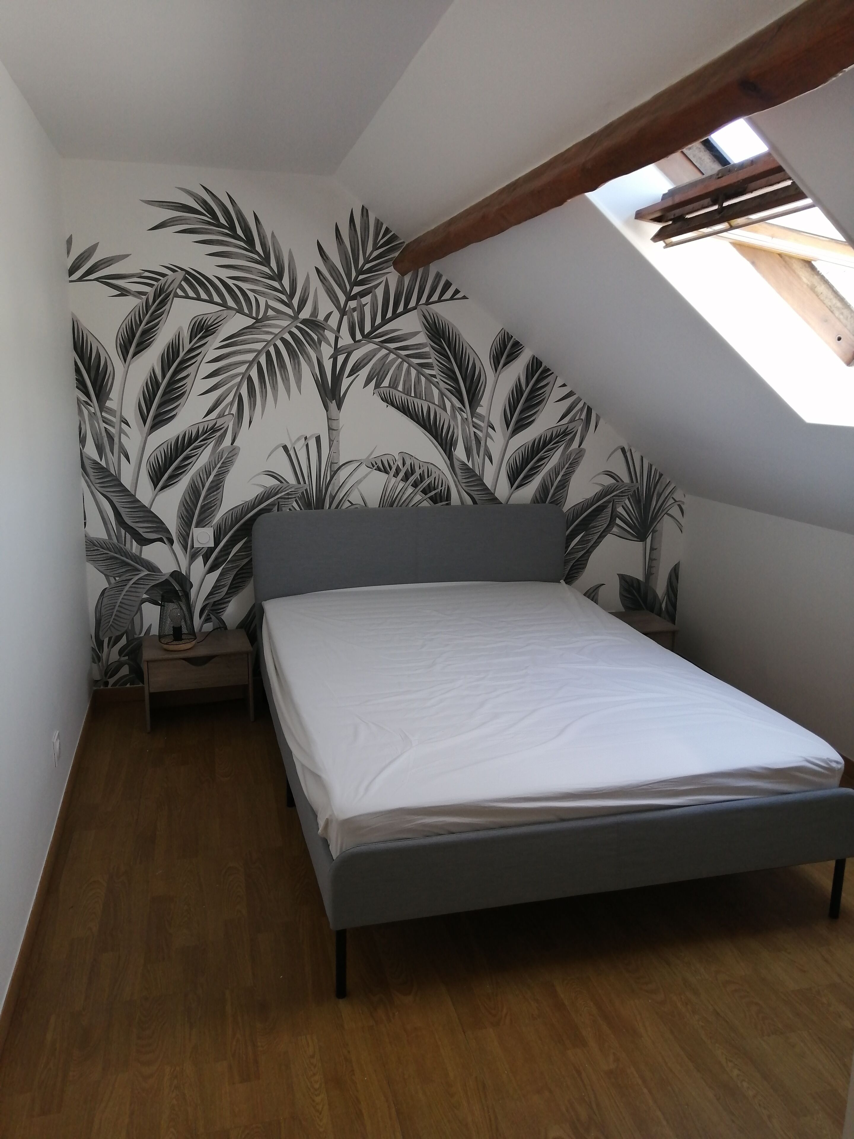 Un dormitorio con techo inclinado, una cama, una mesita de noche y una pared con diseño de hojas.