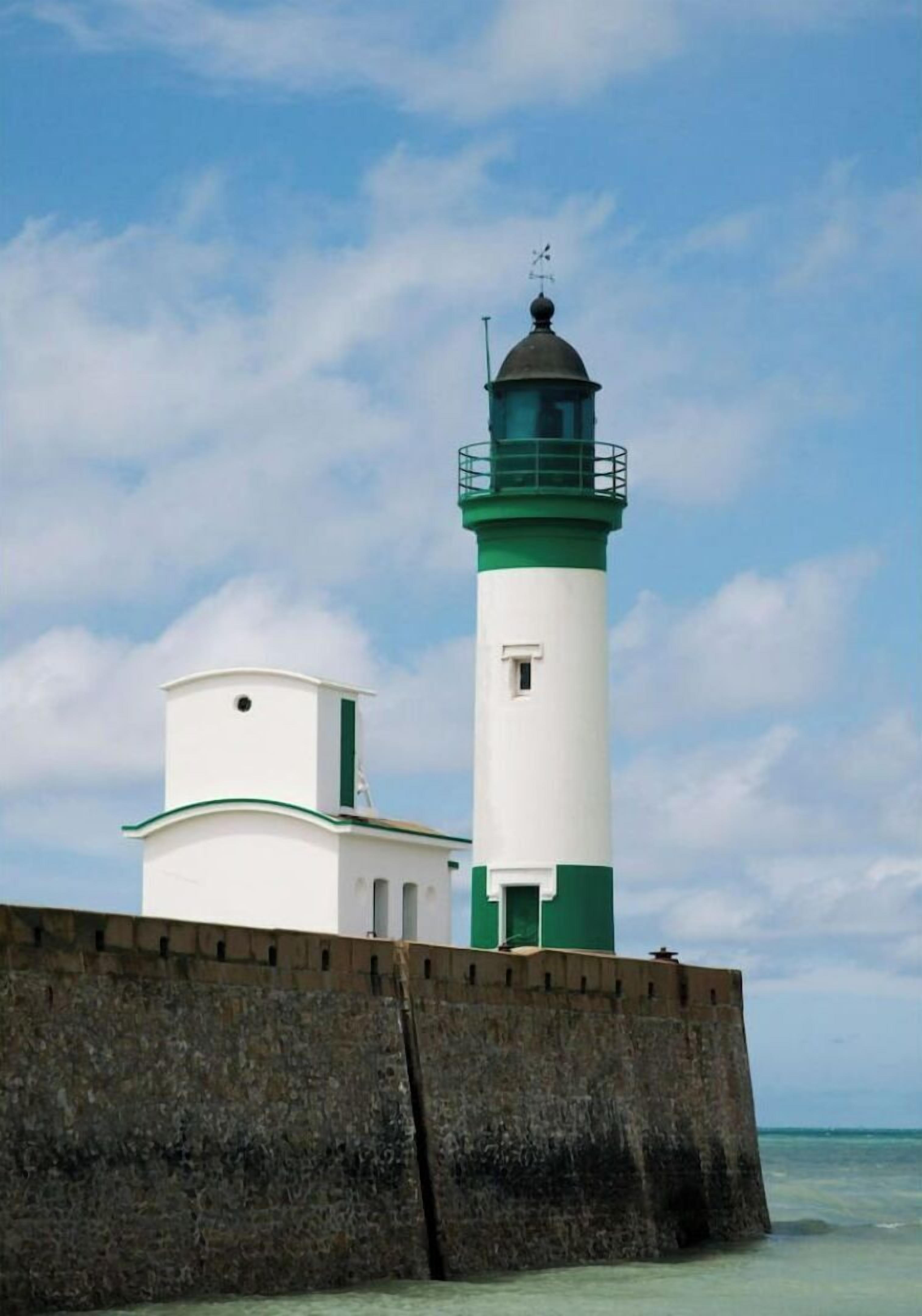 A lighthouse with a white and green exterior, a smaller adjacent building, and a stone wall.