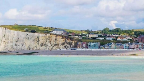 A coastal scene with a beach, cliffs, and buildings in the background.