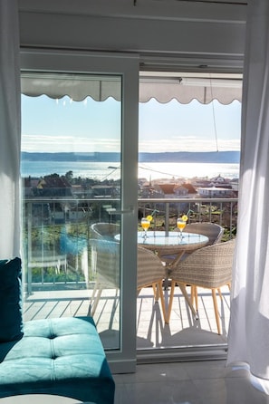 Enjoy the serene view from this balcony with a glass door leading to an outdoor seating area featuring wicker chairs and a glass table.