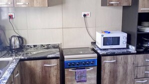 A kitchen with wooden cabinets, a stove, a microwave, and a kettle. - Lovely 2-bedroom Serviced Apartment With a Balcony (Abuja)